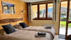 A hotel room with two beds, a wooden headboard, a window with curtains, and a view of the outdoors. - WONDERFUL SPACIOUS CHALET IN BOURG D’OISANS - SLEEPS 10(*supplement available up to 16) (Le Bourg-d'Oisans)