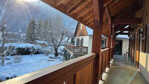 A wooden balcony with a view of a snow-covered landscape and a traditional building. - WONDERFUL SPACIOUS CHALET IN BOURG D’OISANS - SLEEPS 10(*supplement available up to 16) (Le Bourg-d'Oisans)