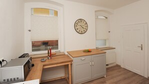 Una cucina compatta con un piano di lavoro in legno, un forno a microonde integrato e una sveglia a muro.