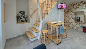 Un espace de vie moderne comprenant un escalier, une table à manger avec des tabourets, un canapé et un mur en pierre.
