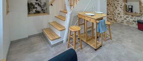 A modern living space with a staircase, a dining table with stools, a sofa, and a stone wall.