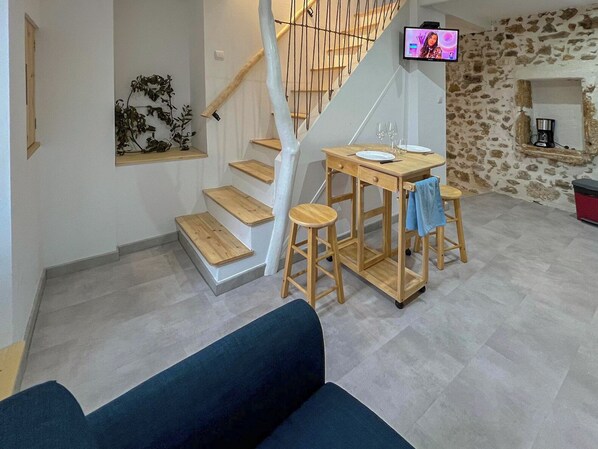 A modern living space with a staircase, a dining table with stools, a sofa, and a stone wall.