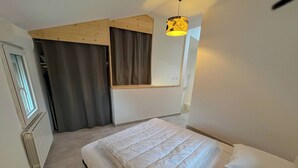 Une chambre à coucher avec un lit, une fenêtre, un radiateur, un plafond en bois et un luminaire suspendu.