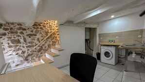 Une cuisine compacte équipée d’un lave-linge, d’une table en bois et d’un escalier en pierre le long d’un mur.