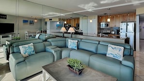 Ein modernes Wohnzimmer mit einem Ecksofa, einem Couchtisch mit Pflanze und einer Küchenzeile im Hintergrund.