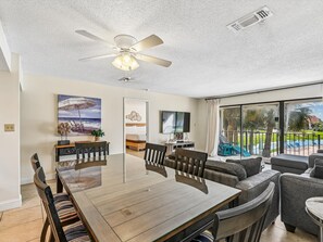 A spacious dining area with a large table and chairs, a ceiling fan, and a view of a pool and greenery outside. - Edgewater Villa #2510 | Golf, Tennis, Beach! (Panama City Beach)