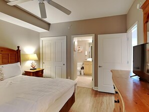 A bedroom with a bed, a nightstand, a lamp, a ceiling fan, and a TV. - Grandview East #1005 | Near Area Fun! (Panama City Beach)