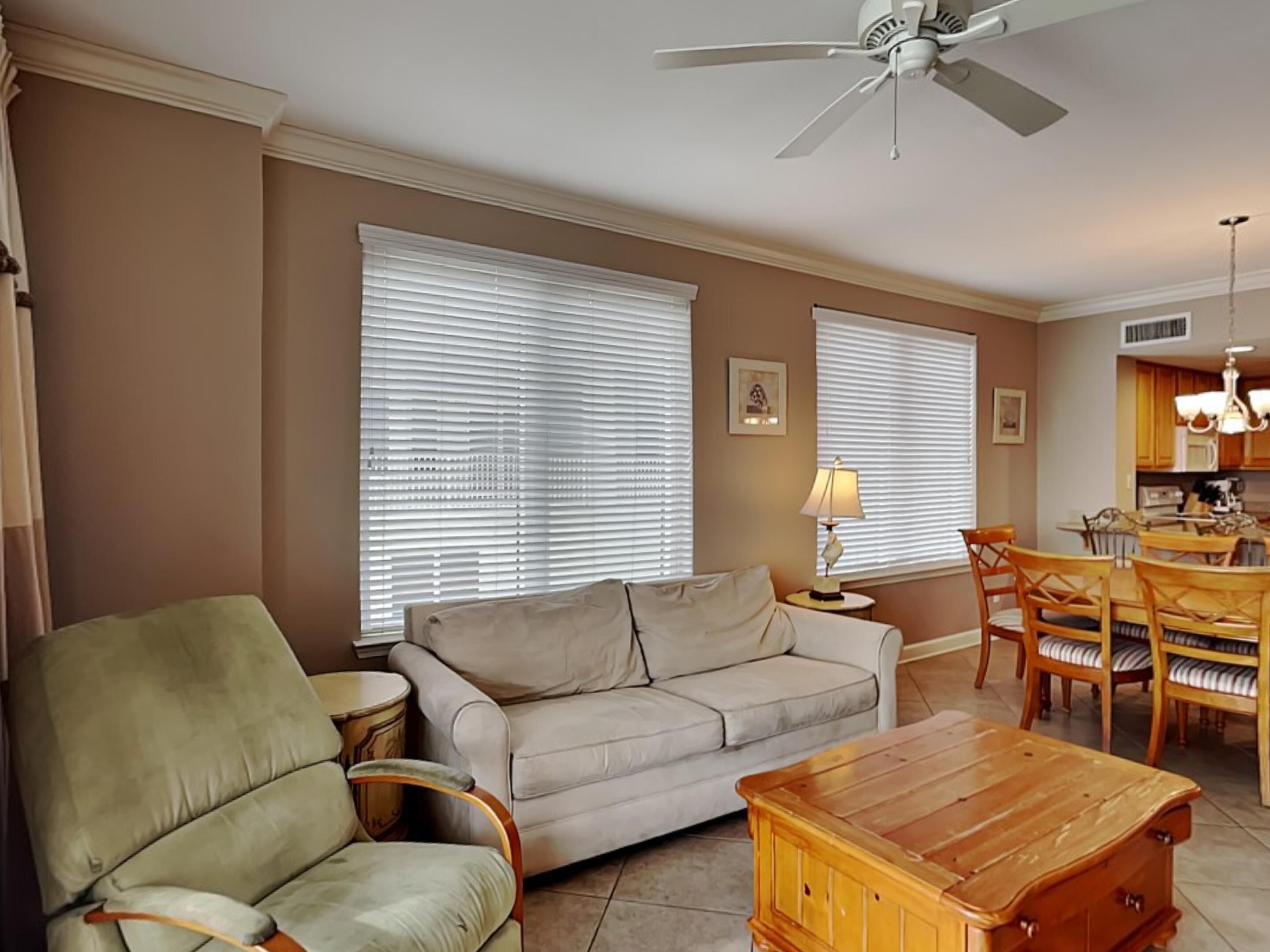 A living room with a sofa, armchair, wooden coffee table, and dining area with chairs and a table.