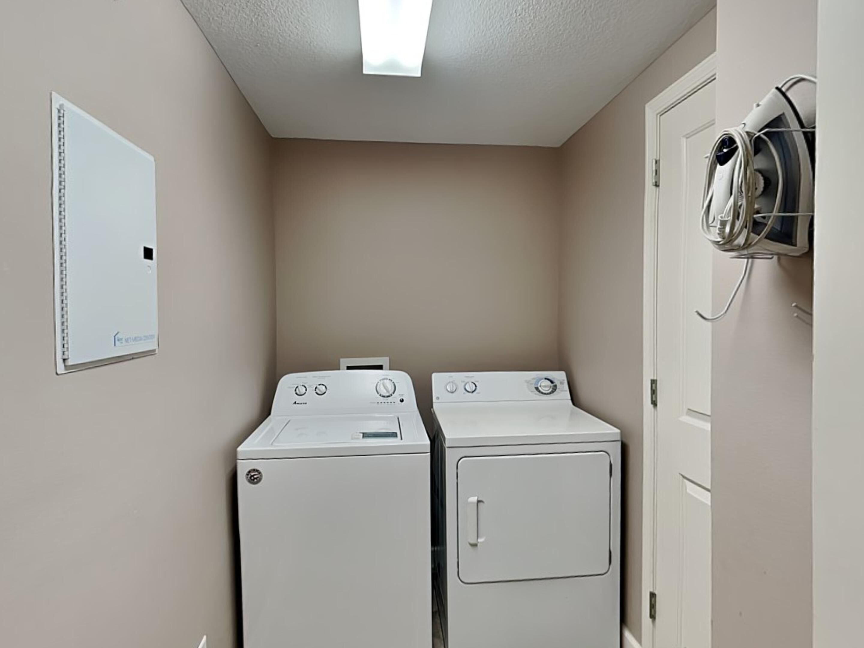 A laundry room with two front-loading washers and dryers, a whiteboard, and a ceiling light fixture.