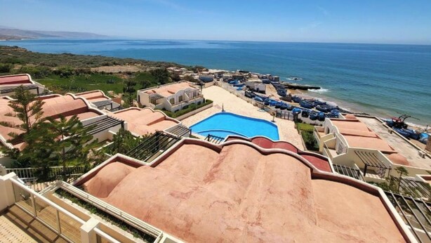 Ein Resort mit Swimmingpool, Liegestühlen direkt am Strand und Blick auf den Ozean.