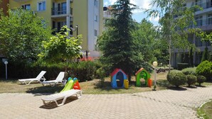 Une cour avec des fauteuils de jardin, des cabanes colorées et un bâtiment en arrière-plan.