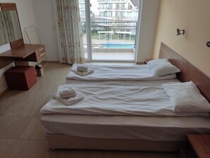 A hotel room with two beds, a wooden dresser, a mirror, and a view of a swimming pool.