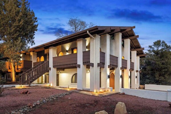 A modern two-story house with a covered patio, large columns, and a staircase leading to the upper level.