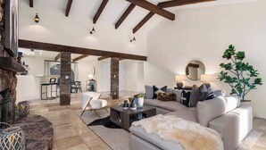 Ein großzügiges Wohnzimmer mit einer breiten Couch, einem Couchtisch und einem Kamin. Im Hintergrund ist eine Essecke mit Tisch und Stühlen zu sehen.