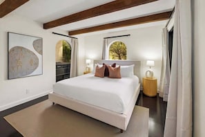 A bedroom with a large bed, two bedside tables, a window with a view, and a painting on the wall.