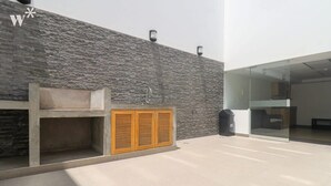 Un espacio exterior moderno con un muro de piedra, un banco de madera y una puerta de cristal que da al interior.