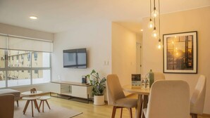 Una sala de estar moderna con televisor, comedor y ventanas amplias.