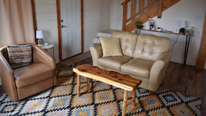 A living room with a leather sofa, a wooden coffee table, a patterned rug, a small side table with a lamp, and a staircase in the background. - Mountain Cabin w/ Stunning Night Skies & 360° Views -Fast WiFi (Westcliffe)