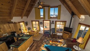 A cozy cabin interior with a kitchen, dining area, and living room, featuring wooden floors and large windows.