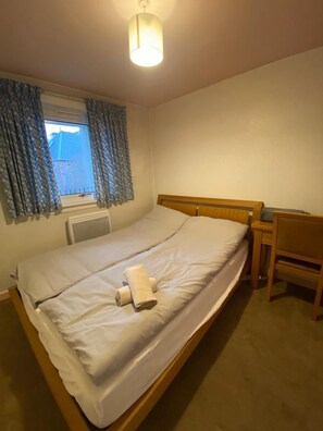 A single bed with a wooden headboard, a bedside table, a chair, and a window with curtains. - EDI B&B (Edinburgh)