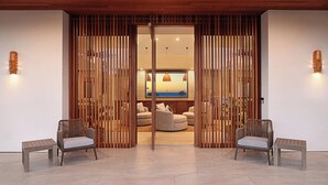 A modern interior with a wooden partition, two wicker chairs, and a round seating area with cushions. - Hula House: Luxury Villa w/ Superb Views/Amenities (Koloa)