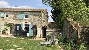 A stone building with a tiled roof, a grassy lawn with stepping stones, and a wooden fence. - A peaceful, restful little corner (Annezay)