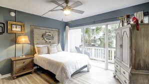 A bedroom with a bed, a nightstand, a lamp, a ceiling fan, a wardrobe, and a view of palm trees through a sliding glass door. - Sunset Rentals | Treetops 5701 | Dog Friendly (Hilton Head Island)