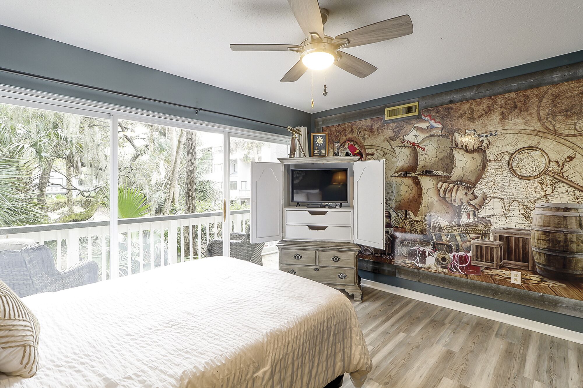 Un dormitorio con una cama grande, un ventilador de techo, un televisor y un mural en la pared.