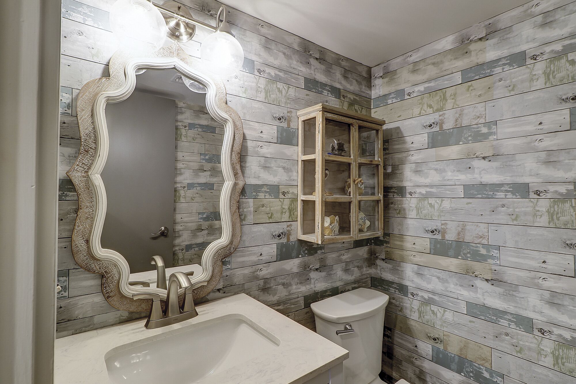 A bathroom with a white sink, a mirror with an ornate frame, a toilet, and a cabinet with glass doors.