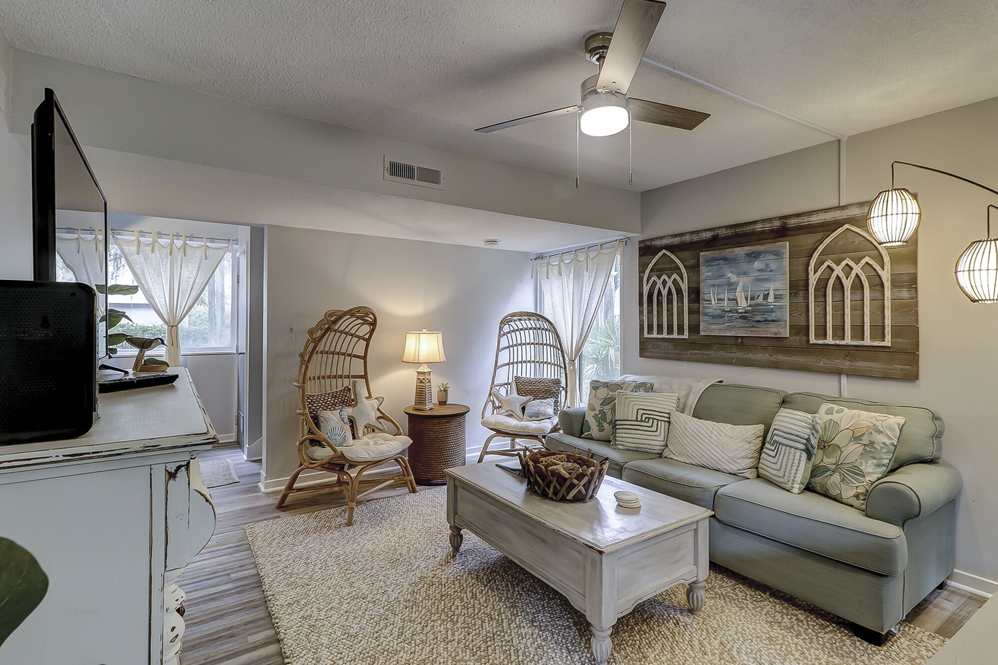 A living room with a sofa, two wicker chairs, a coffee table, and a TV on a stand.