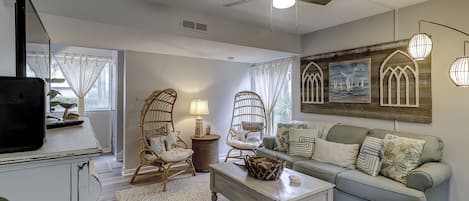 A living room with a sofa, two wicker chairs, a coffee table, and a TV on a stand.