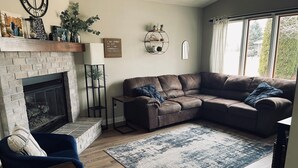 A living room with a fireplace, a brown leather sectional sofa, a blue armchair, and a patterned rug. - Oshkosh EAA AirVenture Rental (Oshkosh)