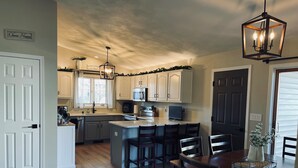 A modern kitchen with white cabinets, a central island, and a dining area with dark wooden chairs. - Oshkosh EAA AirVenture Rental (Oshkosh)