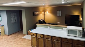 A kitchen with wooden cabinets, a microwave, and a dining area with a chair and table. - Oshkosh EAA AirVenture Rental (Oshkosh)