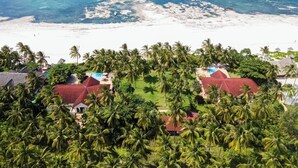 Een luchtbeeld van een resort met meerdere gebouwen, palmbomen en een strand.