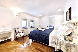 Une chambre à coucher comprenant un lit, une chaise, une petite table avec des livres et une fenêtre donnant sur une salle de bain.