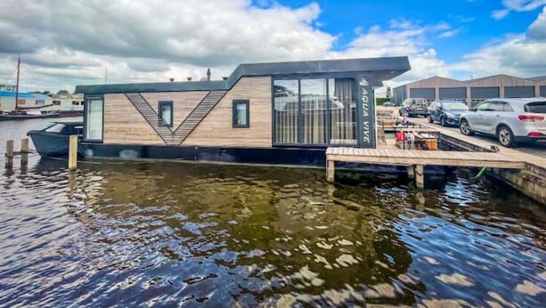 Eine moderne, schwimmende Struktur mit Anlegesteg, genannt 'Aqua Vibe', mit geometrischem Design und großen Fenstern.