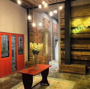 Une pièce avec un mur en bois, un panneau néon, une porte rouge et une table sur laquelle se trouve un vase de fleurs.