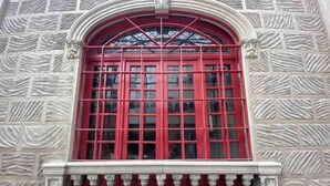 Eine Gebäudefassade mit einem rot gerahmten Fenster, einer Steinwandstruktur und einem Sims.