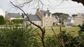 A large stone house with multiple chimneys, a well-maintained lawn, and a gated driveway. - Stone house 300 m from the beach (Plouguerneau)