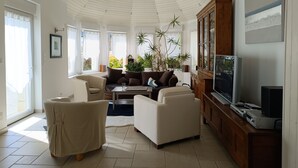 A spacious living room with a high ceiling, a large cabinet, a television, and a sofa. - Stone house 300 m from the beach (Plouguerneau)