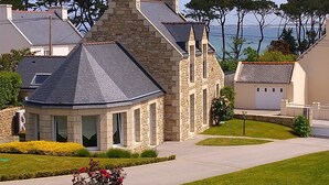 A stone house with a sloped roof, a garage, and a well-maintained lawn. - Stone house 300 m from the beach (Plouguerneau)