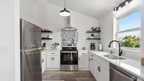 A modern kitchen with white cabinetry, stainless steel appliances, and a large window providing a view of the outdoors.