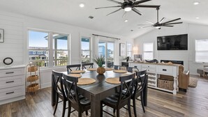 A spacious dining area with a dark wooden table and chairs, surrounded by large windows offering a view of the neighborhood.