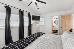 A bedroom with a bed, a ceiling fan, a TV, a dresser, and a door leading to another room.