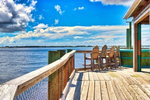 A wooden deck with a view of the water, a table with chairs, and a building with a green roof.