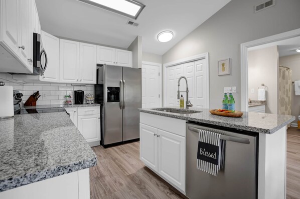 A modern kitchen with white cabinets, granite countertops, stainless steel appliances, and a central island with a towel rack.