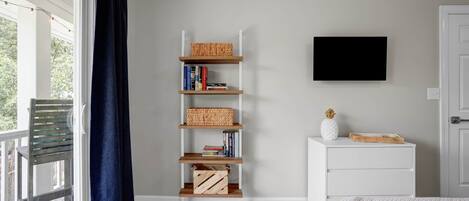 Een slaapkamer met een boekenkast, een flatscreen-tv en een raam met gordijnen.