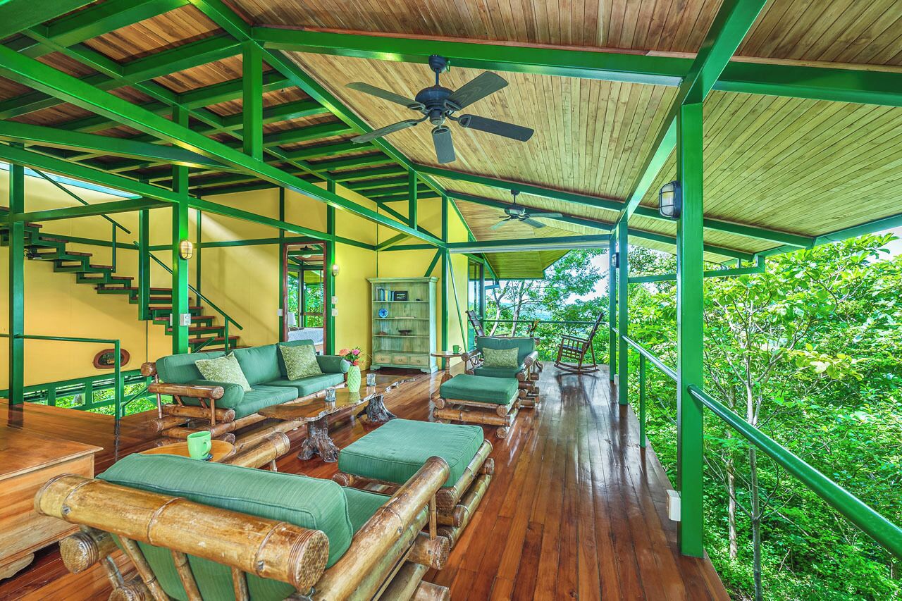 A wooden deck with green furniture, a ceiling fan, and a staircase.