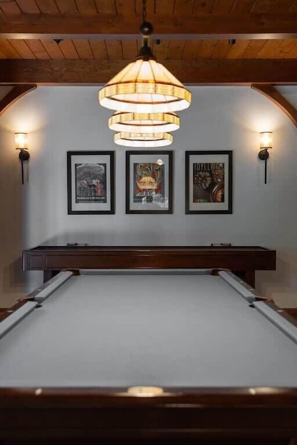 A pool table with a wooden frame, a hanging lamp, and three framed pictures on the wall.